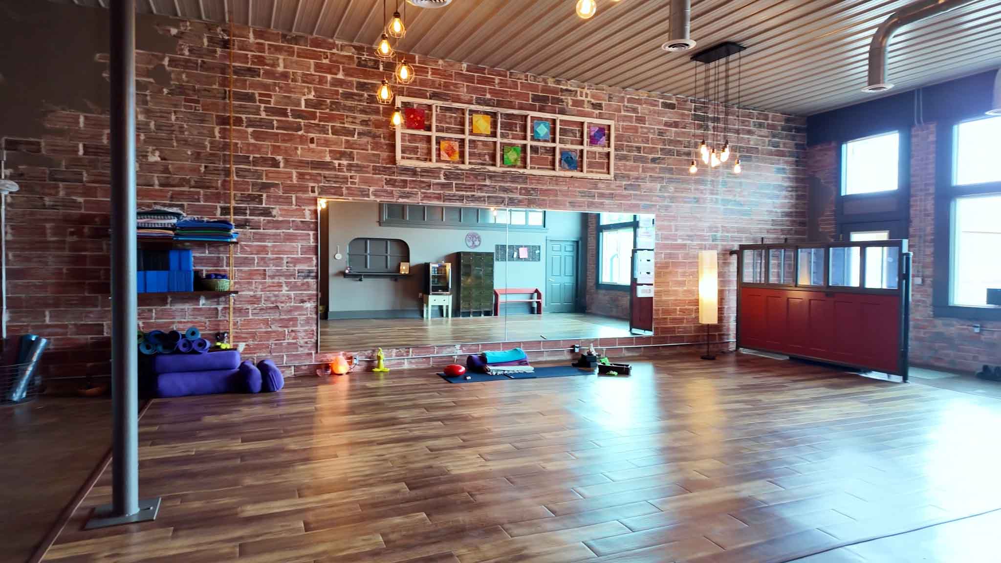 The studio at 627 Market Street — exposed brick, a mirrored wall, wood floors, hanging Edison lights and mats laid out ready for class.