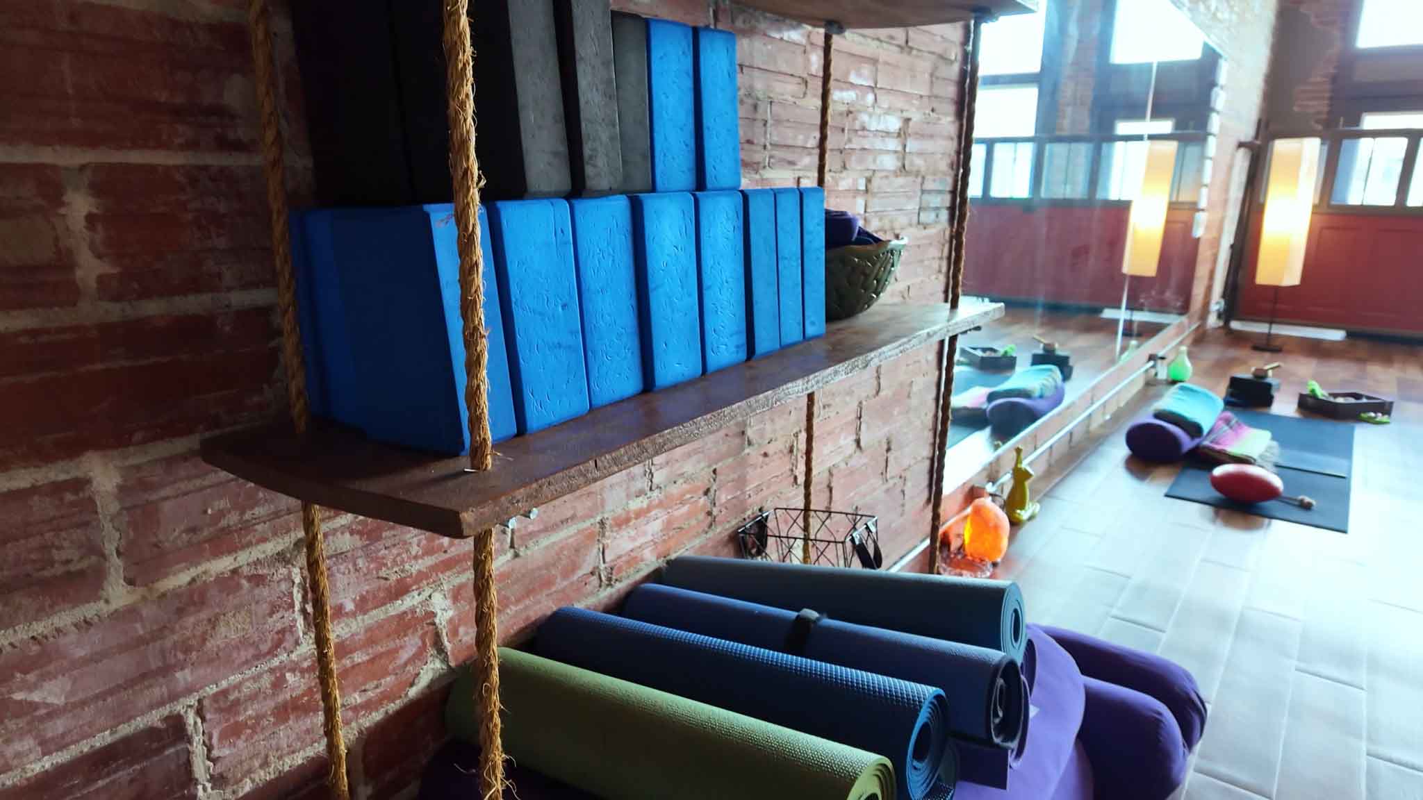 Foam blocks, rolled mats and bolsters on the studio&rsquo;s reclaimed-wood shelving against exposed brick — the studio supplies every prop.