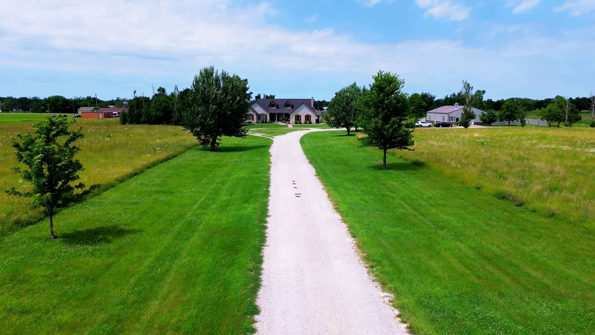 The gravel drive leading in to the retreat property, lined with young trees, with the house ahead.