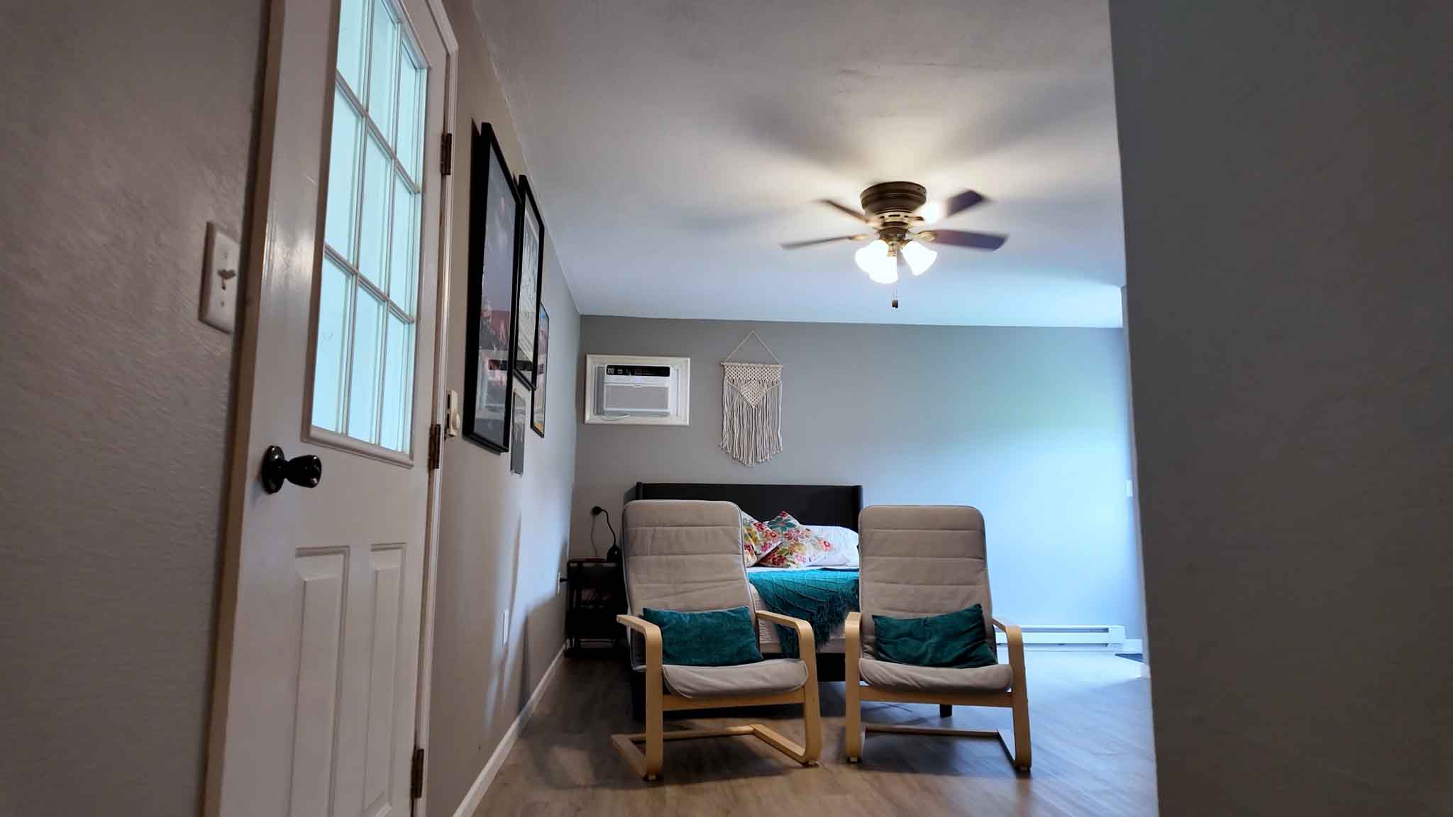 Inside the private guest accommodation — a Queen bed with two cushioned armchairs and a macramé hanging on the wall.